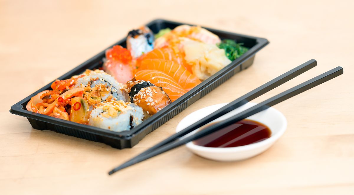 Torched trout and rice pieces arranged in a black tray with soy