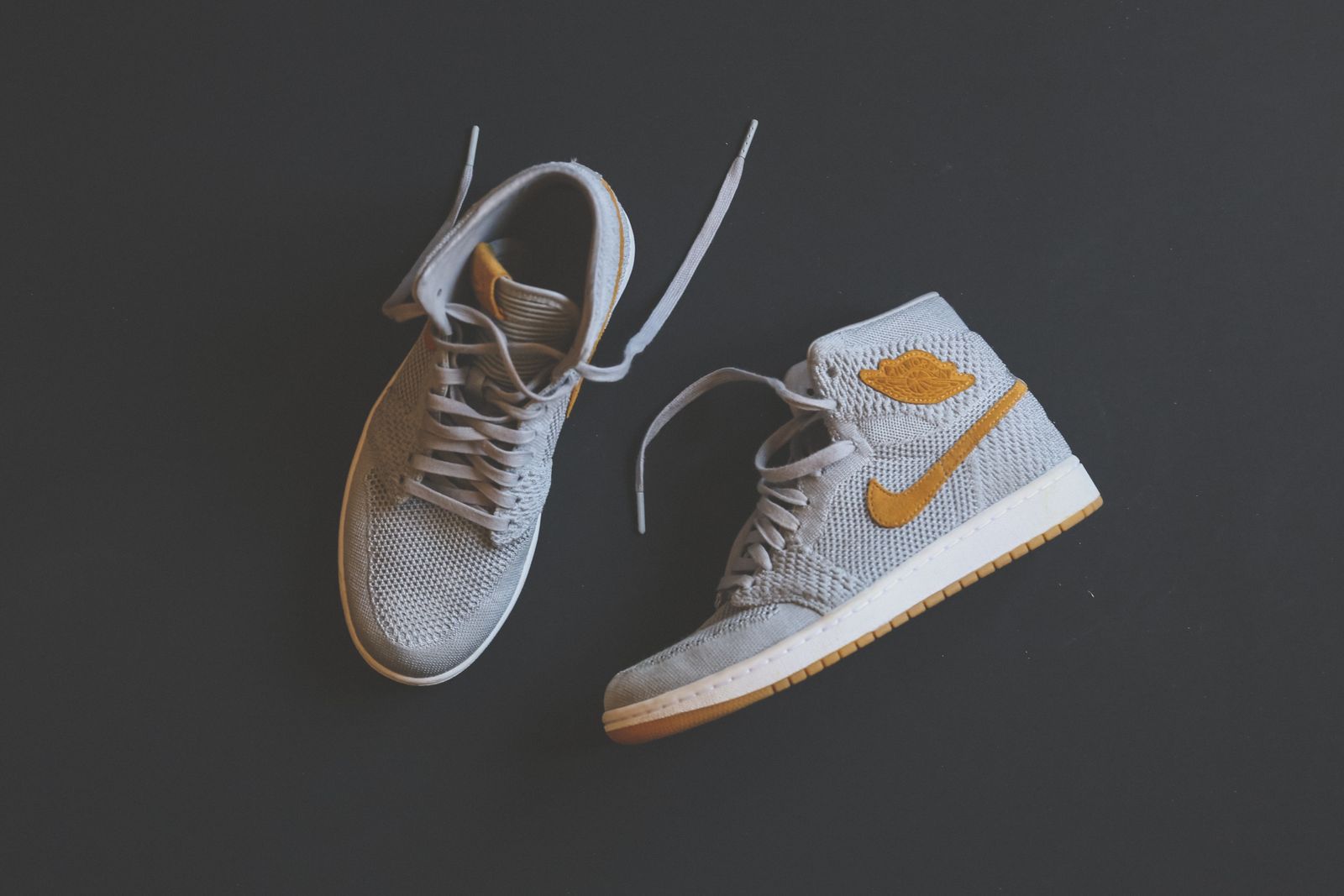 Grey knit high-tops with mustard swoosh on dark surface