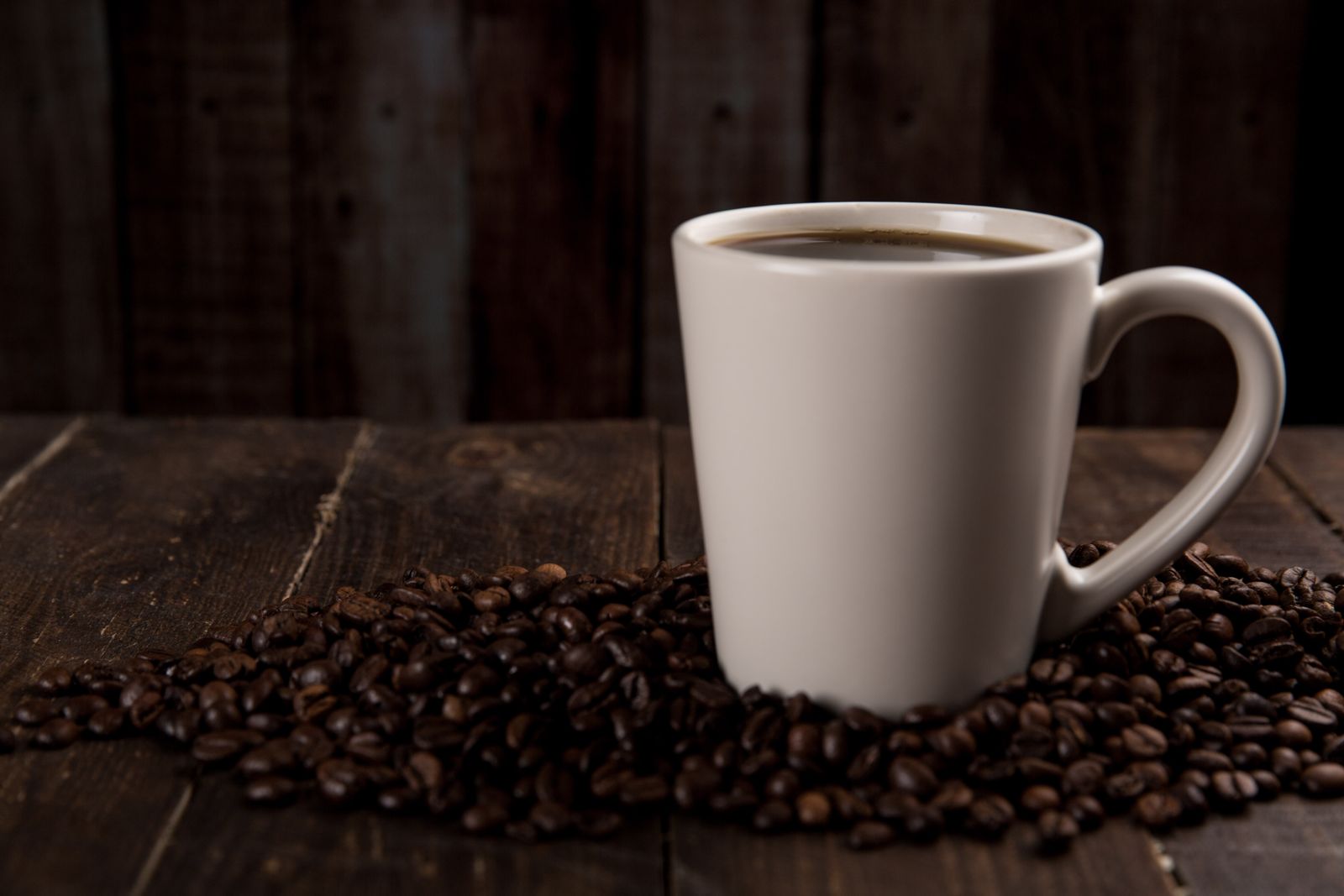 Black coffee in white mug surrounded by beans