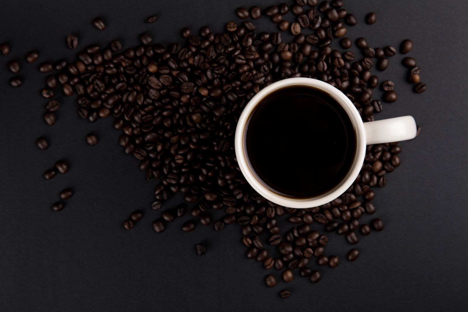Top-down view of coffee mug on black surface with beans